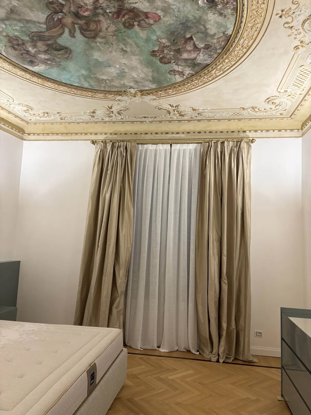 Tende doppie color sabbia sotto un soffitto affrescato con cornice dorata